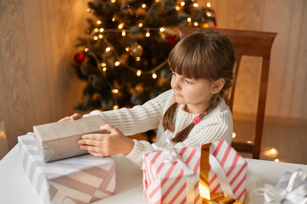 Menina embalando presentes de natal, sentada à mesa