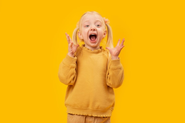 Menina emocional grita Criança pré-escolar fica surpresa Retrato de menina de terno amarelo sobre fundo amarelo
