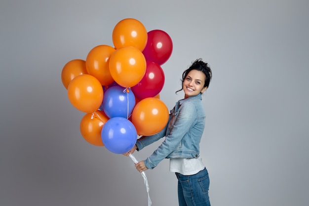 Menina encantada sorridente em jeans posando com balões de ar coloridos brilhantes, isolados no cinza