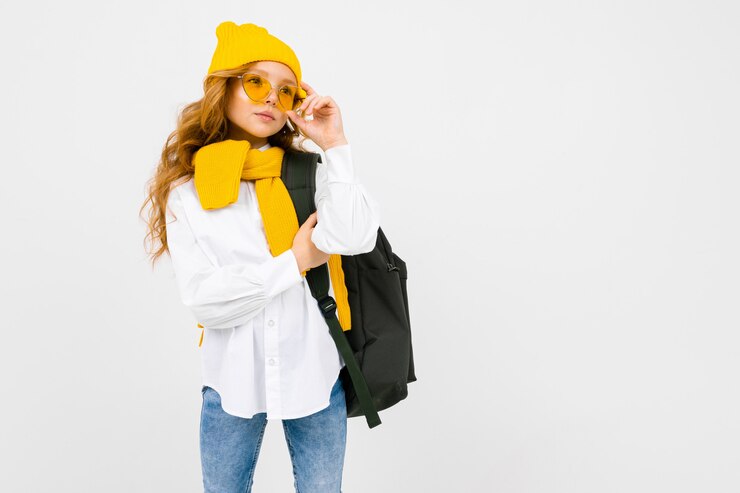 Foto menina encantadora caucasiana elegante em uma camisa branca, calça, um chapéu amarelo, com uma mochila nos ombros, posando em branco, com espaço de cópia