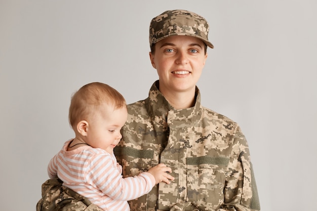 Menina encantadora com sua mãe militar, soldado mulher segurando sua filha, sorrindo, vestindo uniforme do exército, reunião de família, maternidade e voltando para casa da guerra.