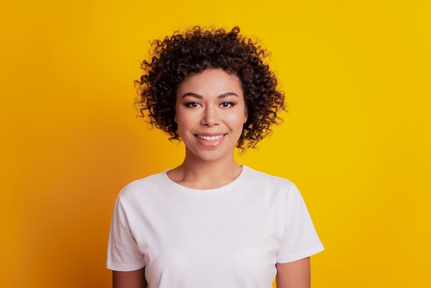 Menina encantadora com um sorriso radiante olhando para a câmera em fundo amarelo