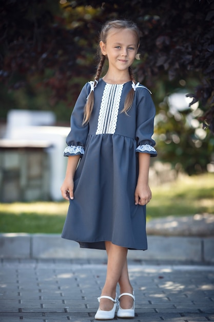 Menina encantadora com um vestido retrô, andando na cidade em um dia ensolarado de verão. Menina usa uniforme escolar. Menina da escola primária com cabelo comprido. Estudo e educação.