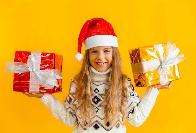 Menina encantadora com uma camisola de malha e um chapéu de Papai Noel com um presente em um fundo amarelo.