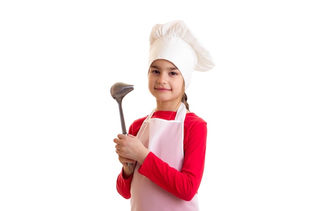 Menina encantadora de camisa vermelha com avental branco e chapéu segurando utensílios de cozinha em estúdio