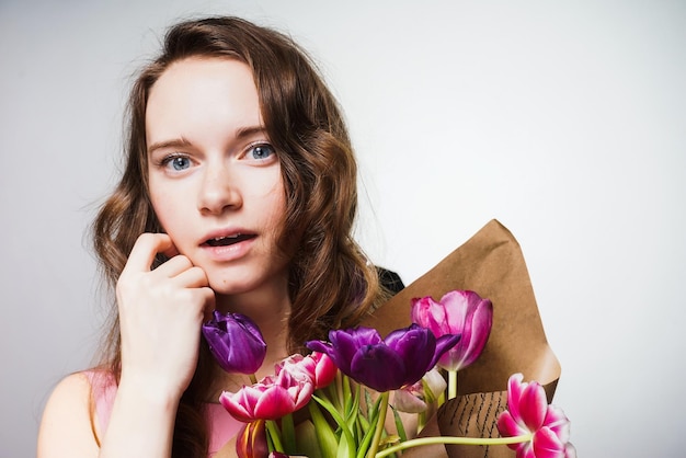 Menina encantadora de olhos azuis com um lindo cabelo comprido segurando um buquê de flores e olhando para a câmera