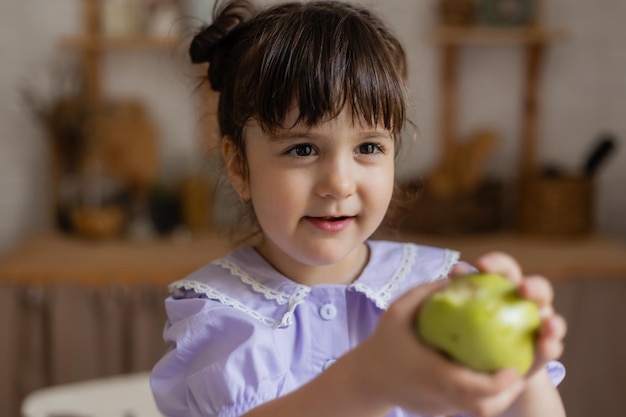 menina encantadora em um vestido lilás come uma maçã verde na cozinha. espaço para texto, banner