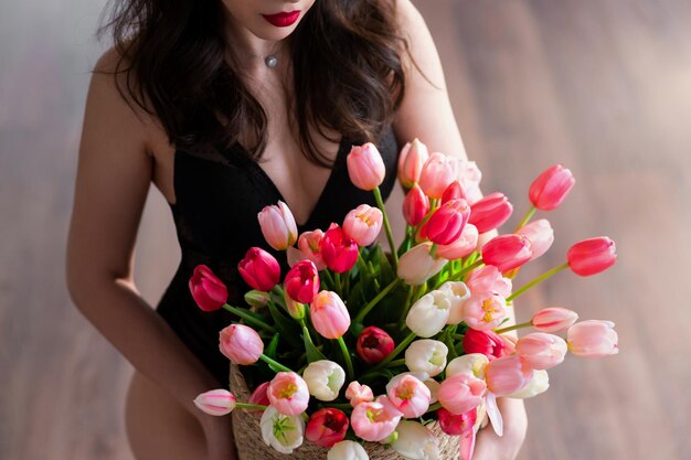 Menina encantadora em uma roupa preta fica em uma sala e segura uma cesta com tulipas coloridas em suas mãos Closeup