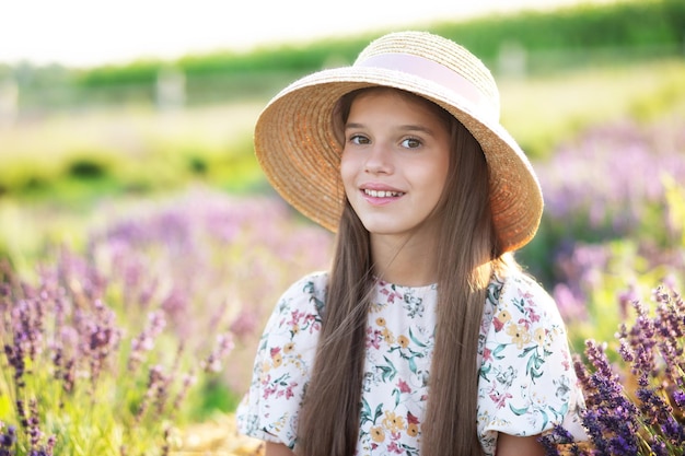 Menina encantadora romântica com cabelo comprido e chapéu de palha grande de verão, senta-se no campo de lavanda