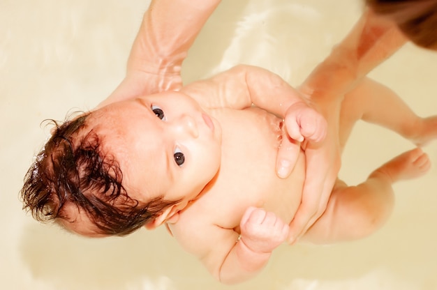 Foto menina encantadora se banha em água morna na banheira nas mãos carinhosas de uma mãe não identificada. o conceito de amor e carinho por criancinhas inocentes