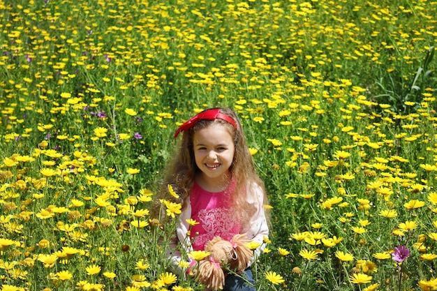 Menina encaracolada com um laço vermelho no cabelo Menina em um prado verde entre flores amarelas