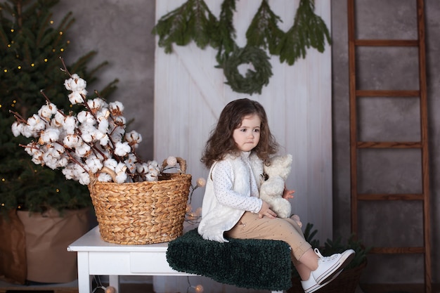 Menina encaracolada com um presente de Natal perto da árvore de Natal na sala de estar