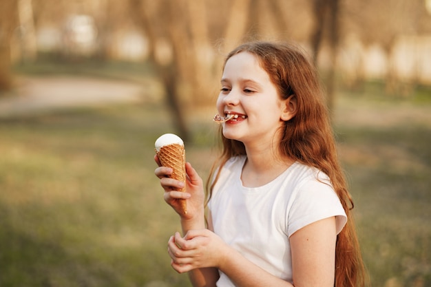 Menina encaracolada come sorvete no parque de verão