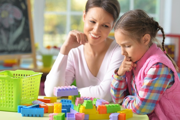 Menina encaracolada e sua mãe brincando com blocos de plástico coloridos