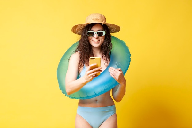 Menina encaracolada em um maiô azul com um anel de natação inflável segura o smartphone nas mãos