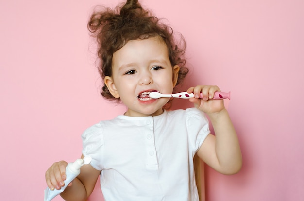 Menina encaracolada escova os dentes com creme dental. treinamento de higiene pessoal para a criança. Garoto boca limpa. Procedimento rotineiro do banheiro em casa.