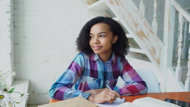 Menina encaracolada sentada à mesa concentrando lições de aprendizagem focadas para exame