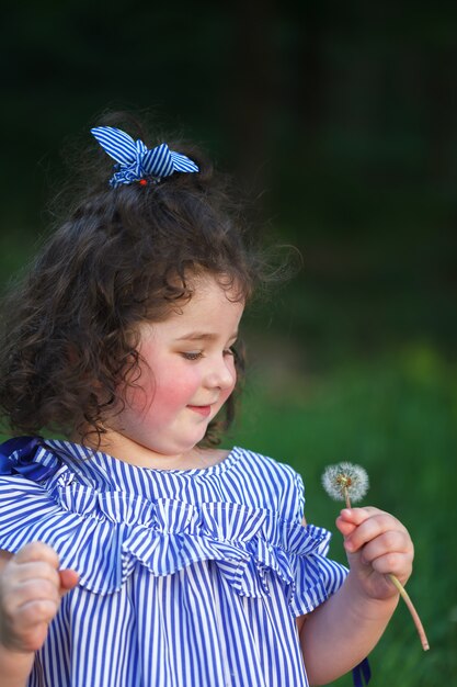 Menina encaracolado bonita pequena que funde em um dente-de-leão.