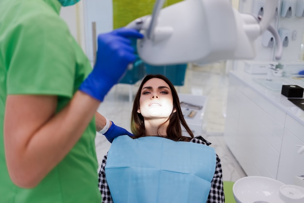 Menina encontra-se em uma cadeira na consulta do dentista. Médico dentista coloca uma lâmpada nos dentes do paciente