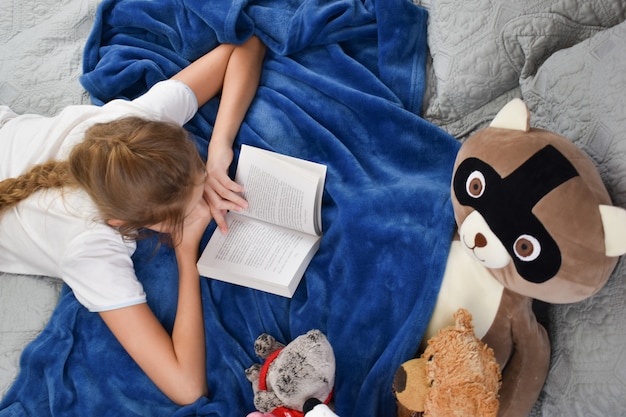 menina encontra-se na cama com um livro e brinquedos