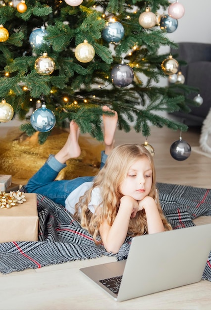 Menina encontra-se perto da árvore de Natal com um laptop. Árvore de Natal em uma grande sala de estar.