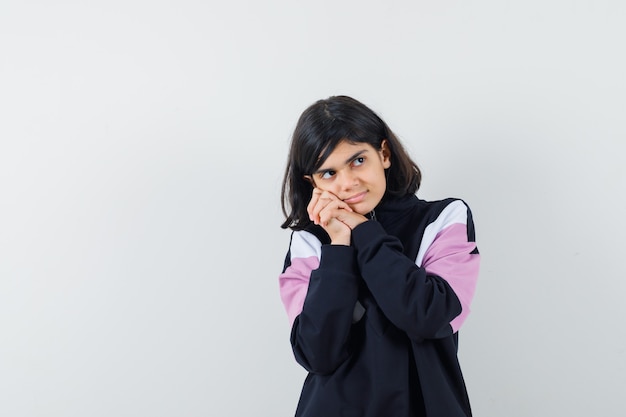 Menina encostando a bochecha nas mãos entrelaçadas na camisa e parecendo um sonho, vista frontal.