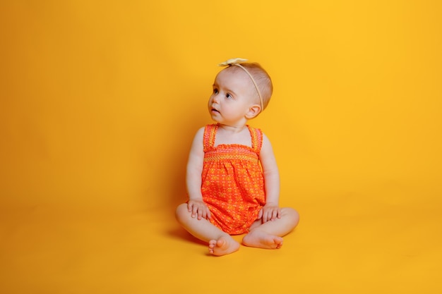 Menina engatinhando em um fundo amarelo segurando uma flor