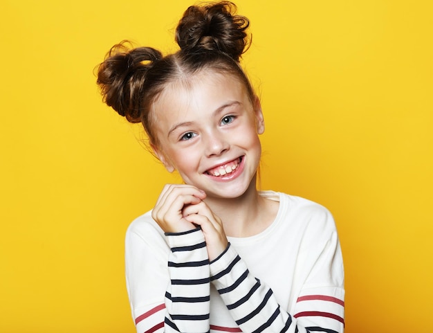 Menina engraçada com cabelo loiro encaracolado rindo olhando na câmera com expressão satisfeita sobre fundo amarelo