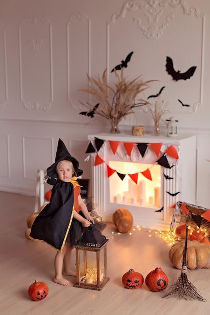 Menina engraçada com fantasia de bruxa de halloween com jack abóbora e vassoura dentro de casa