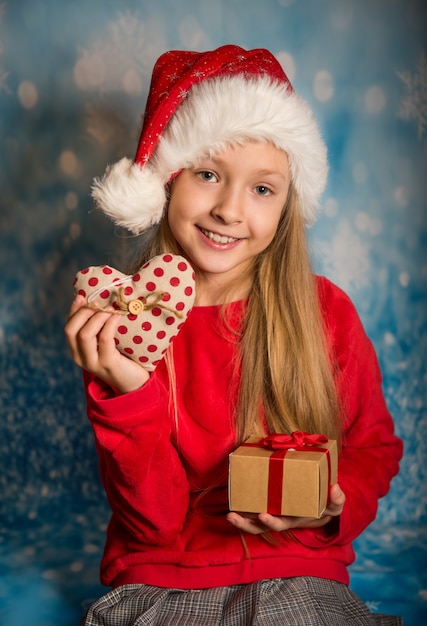 Menina engraçada com lindo chapéu de Papai Noel vermelho segurando uma caixa de presente