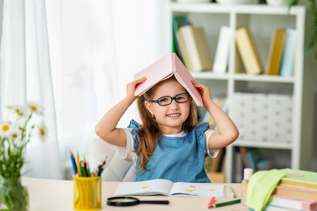 Menina engraçada com óculos e livro na cabeça