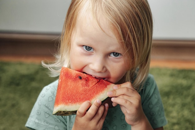 Menina engraçada comendo close-up de melancia. Linda criança com melancia dentro de casa. Conceito de alimentação saudável, verão. Copie o espaço