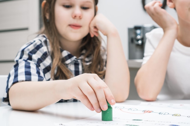 Menina engraçada contemplativa segurando a pata de brinquedo verde como  peça no jogo de tabuleiro acima do mapa na mesa jogos de negócios  familiares