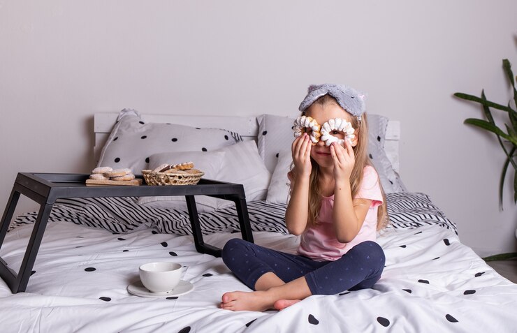 Foto menina engraçada de pijama sentada na cama com uma bandeja de pães