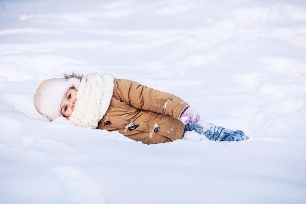 Menina engraçada deitada na neve no inverno