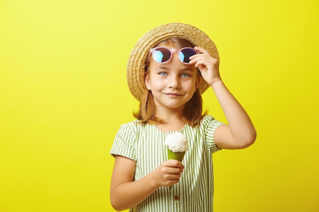 Menina engraçada em roupas de verão comendo sorvete em pé sobre fundo amarelo isolado