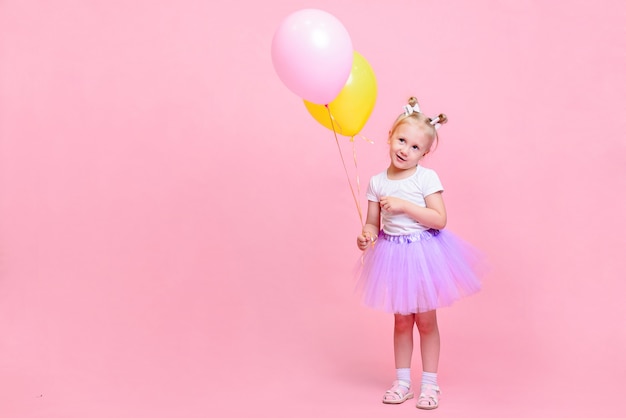 Menina engraçada na camiseta branca e saia lilás com balões em fundo rosa. Retrato infantil com espaço para texto.
