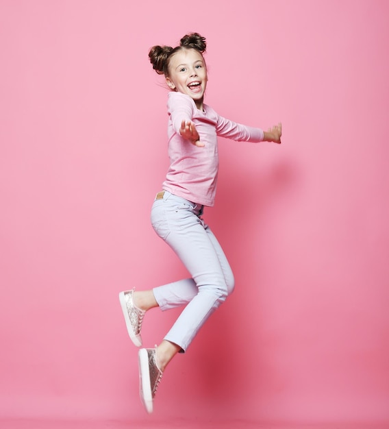 Menina engraçada vestida casualmente pulando no fundo rosa