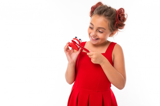 Menina ensina a escovar os dentes em um fundo branco, tem nas mãos uma escova de dentes e um layout dental da mandíbula com dentes