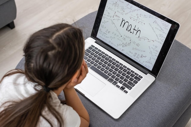 Menina entediada com laptop em casa. Criança bonita fazendo lição de casa no computador. Conceito moderno de educação, comunicação e tecnologia online, espaço de cópia.