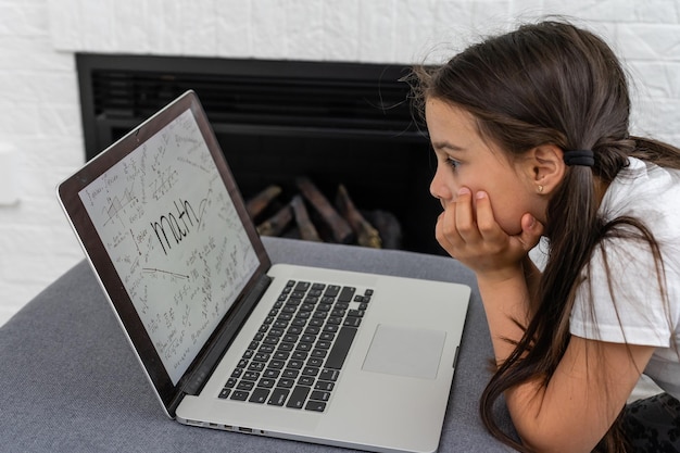 Menina entediada com laptop em casa. Criança bonita fazendo lição de casa no computador. Conceito moderno de educação, comunicação e tecnologia online, espaço de cópia.