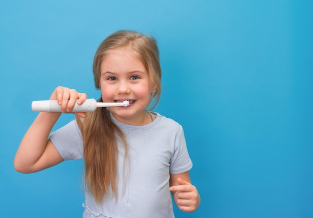 Menina escovando os dentes com escova elétrica em fundo azul com espaço de cópia