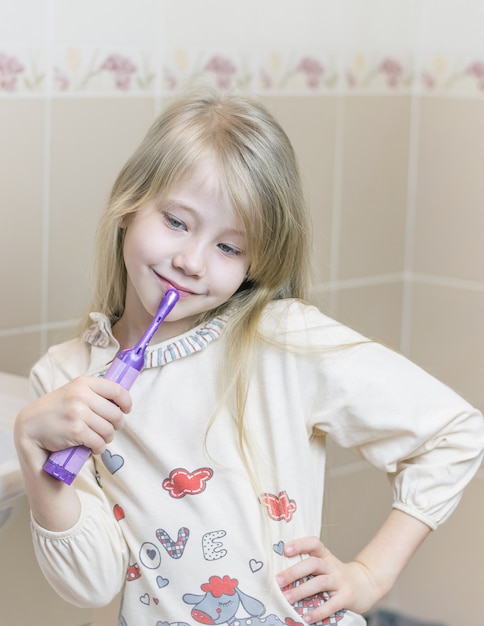 Menina escovando os dentes no banheiro com os olhos baixos.