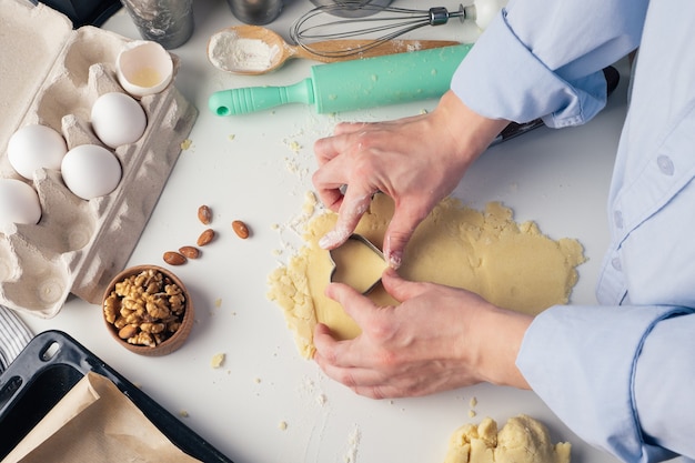 Menina esculpe biscoitos em forma de coração na cozinha, em casa, close-up. Pastelaria artesanal com amor para o Dia dos Namorados, Dia das Mães ou Dia dos Pais. Fundo culinário. Comida de férias.