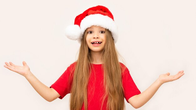 Menina espalha as mãos para o lado em uma parede branca no dia de Natal.