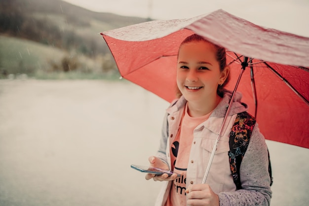 Menina esperando ônibus em dia de chuva e usando telefone