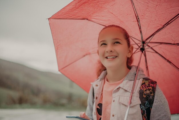 Menina esperando ônibus em dia de chuva e usando telefone