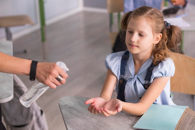 Foto menina esperando para desinfetar as mãos na sala de aula