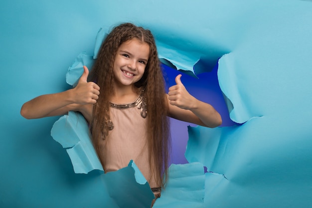 Foto menina espiando por um buraco no papel azul