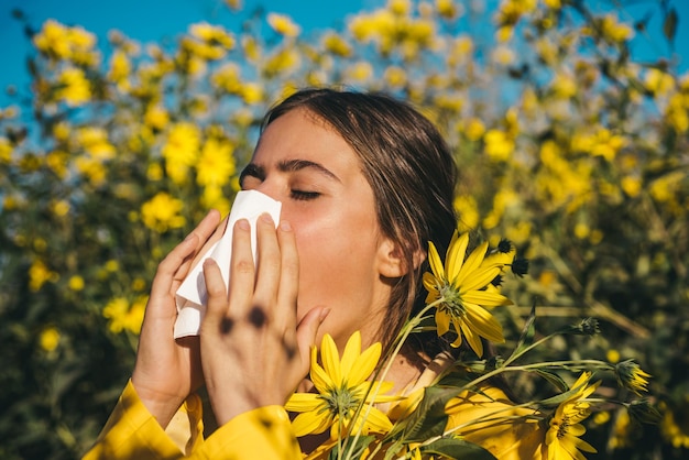 Menina espirrando e segurando lenço de papel em uma mão e buquê de flores em outra jovem tem